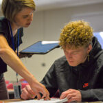 Female instructor interacting with a male student at his desk