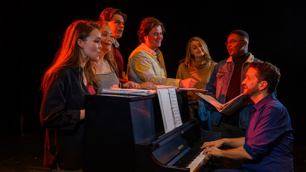 UNCG faculty member playing piano with students singing around him