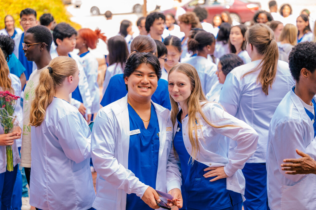 Two nursing students in lab coats and scrubs smiling for the camera