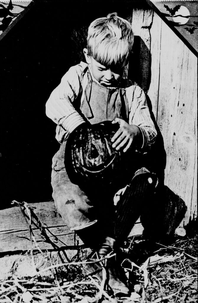 Image detail from a 1915 newspaper depicting a boy carving a pumpkin, showcasing the early American tradition of pumpkin carving for Halloween.