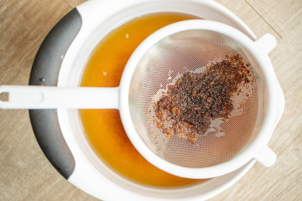 Strainer of cooked beef fat over a bowl of rendered beef tallow.
