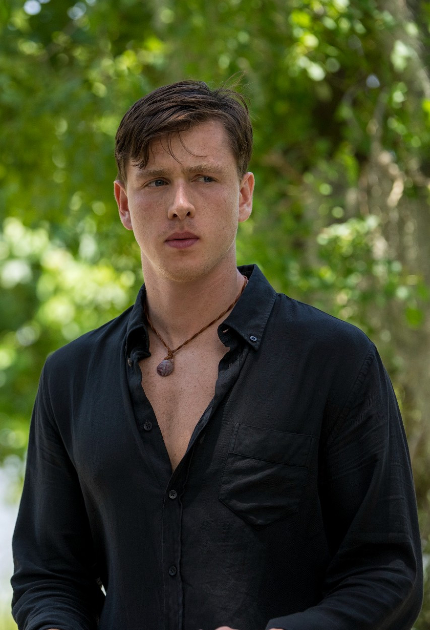 Harris Dickinson as Chase Andrews in Where the Crawdads Sing film, standing confidently in a boat in the marsh.