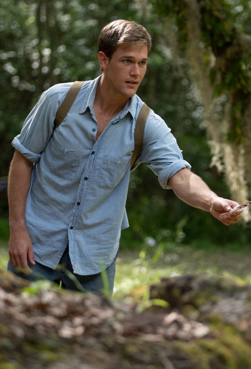 Taylor John Smith as Tate Walker in Where the Crawdads Sing film, holding a feather in the marsh.