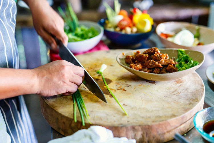 Woman cutting vegetables in kitchen, illustrating cost-effective food preparation.