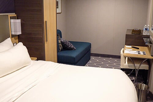 Interior stateroom on Symphony of the Seas featuring a king-sized bed, couch, desk/vanity area, and well-organized closets, designed for comfort and efficiency