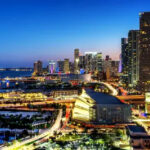 Miami downtown at night with illuminated buildings and reflections in the water, emphasizing the city's vibrant nightlife and urban appeal