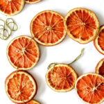 Overhead image of dried orange slices strung together with green string, spiraled on a white counter, creating festive holiday decor.