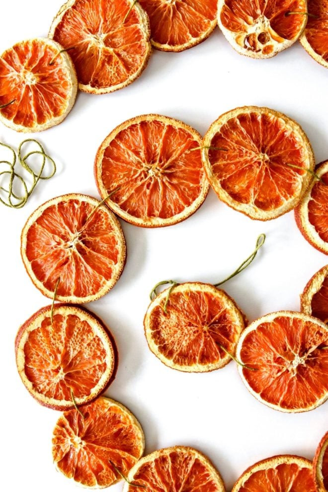 Overhead image of dried orange slices strung together with green string, spiraled on a white counter, creating festive holiday decor.