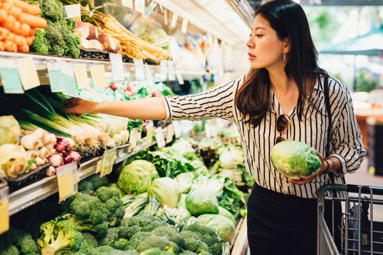 Woman carefully selecting fresh produce at a grocery store.